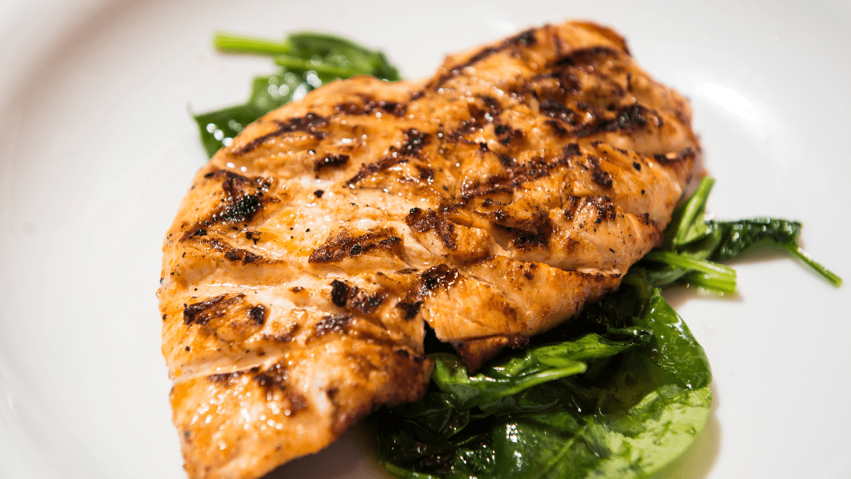 A vibrant, close-up image of grilled chicken breasts with a colorful spice rub, garnished with fresh herbs and served alongside white rice and peas on a rustic plate.
